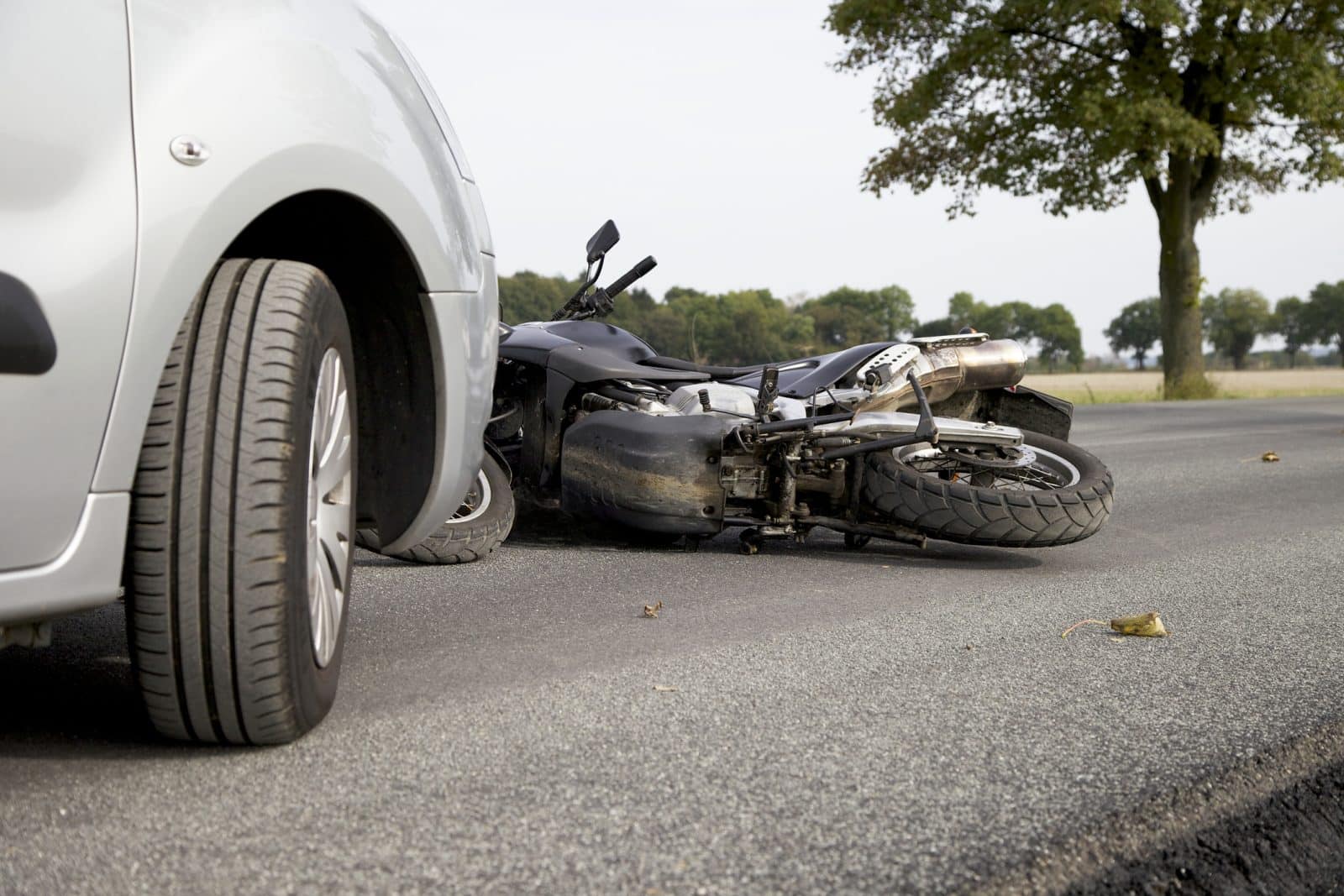 Motorcycle lying on its side on the road after a collision with a silver car, with visible damage to the bike.