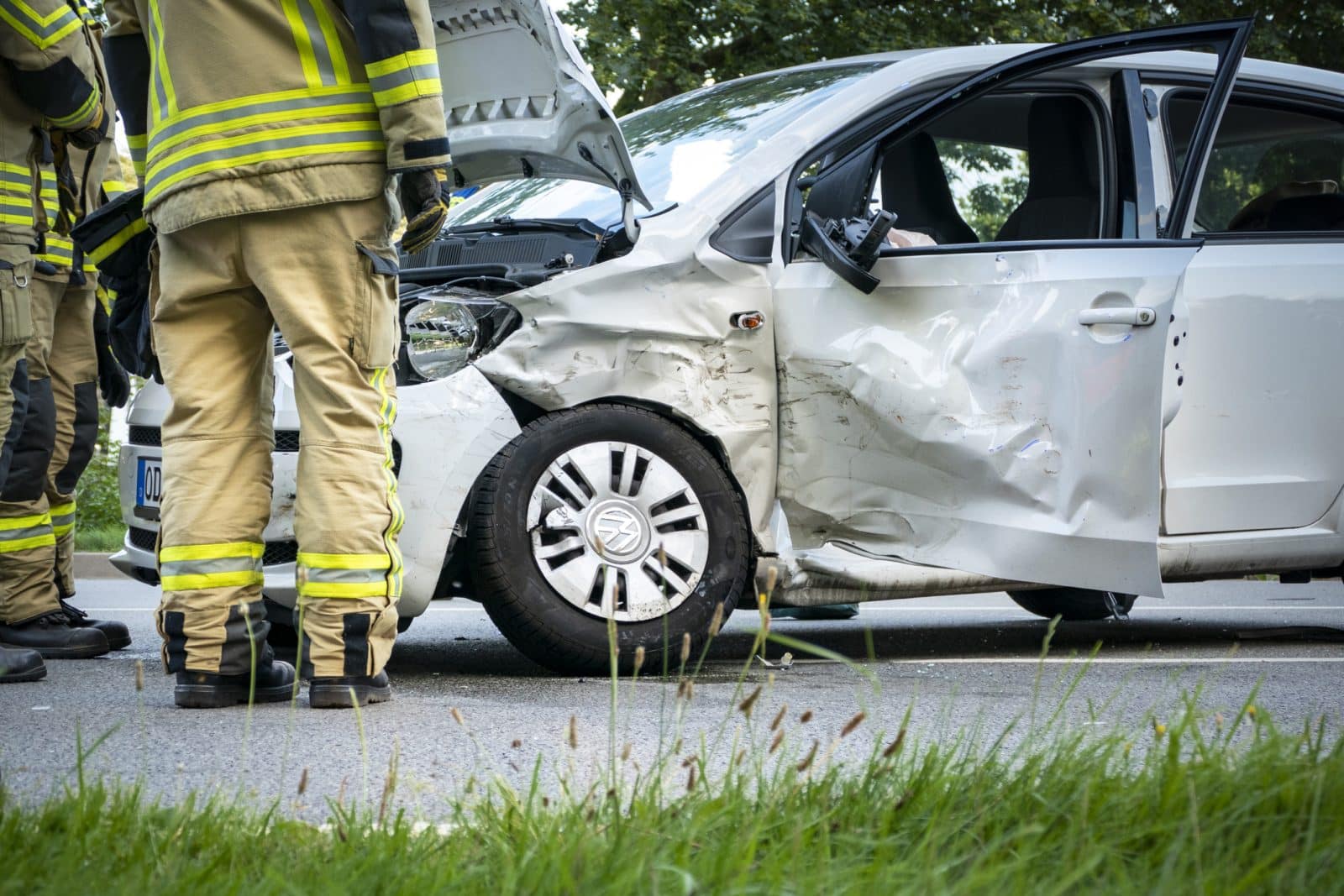 A first responder at the scene of a car accident looking at extensive damage to the side of a silver car.