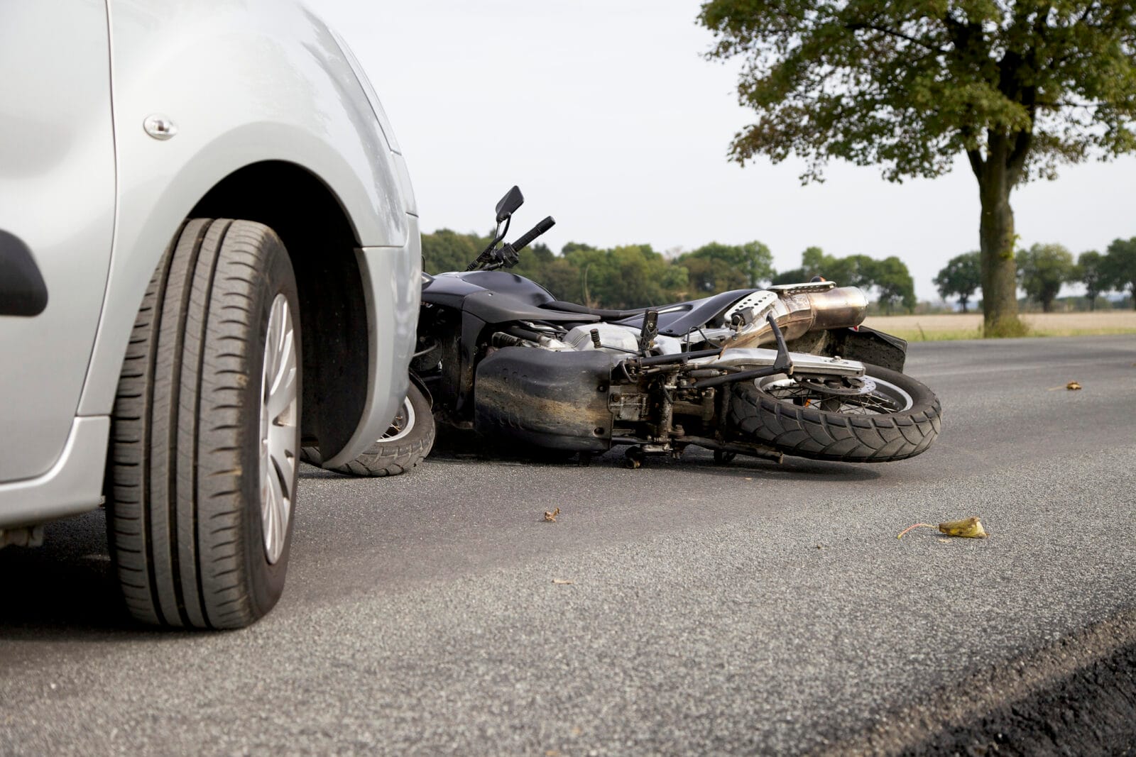 Motorcycle lying on its side on the road after a collision with a silver car, with visible damage to the bike.